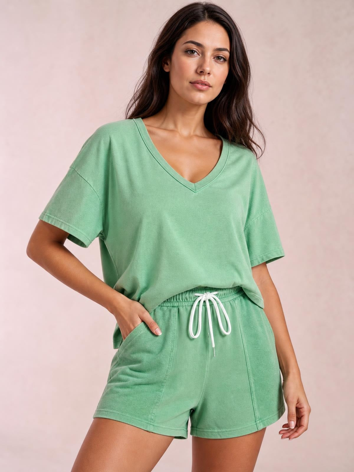 Model poses in a mint green V-neck short sleeve loose top and matching drawstring shorts set with relaxed silhouettes, seam details, and pockets.