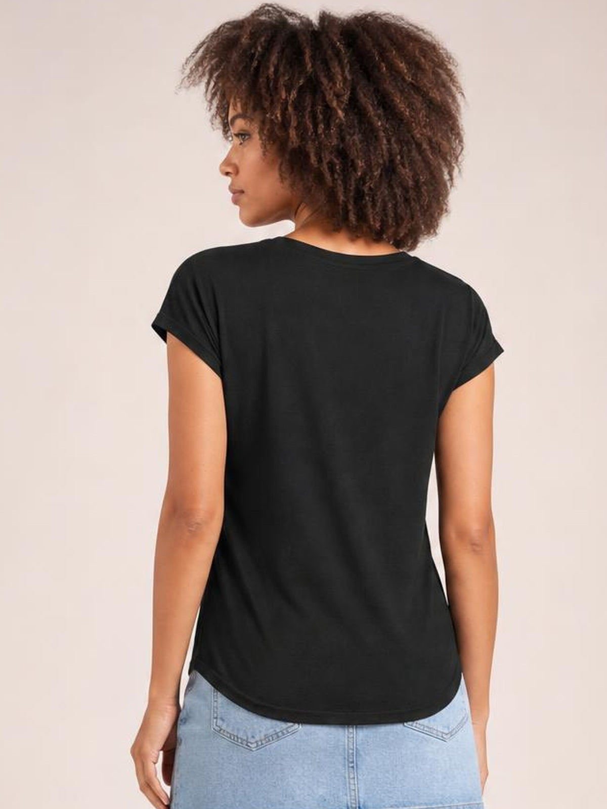 A model faces away wearing a black short-sleeve T-shirt with a relaxed silhouette, turned sleeve cuffs, and a gently curved hem.