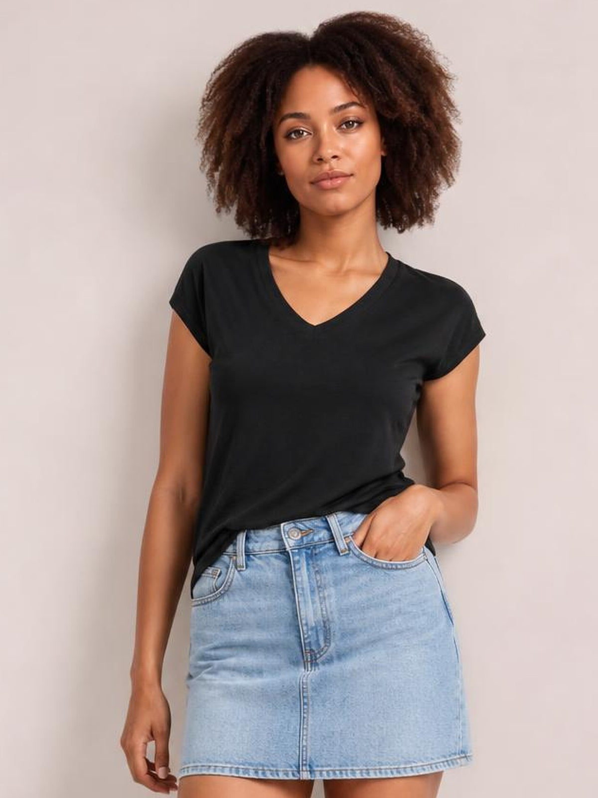 Model wears a black V-neck short sleeve T-shirt with a relaxed straight silhouette, standing with one hand in her light blue denim skirt pocket.