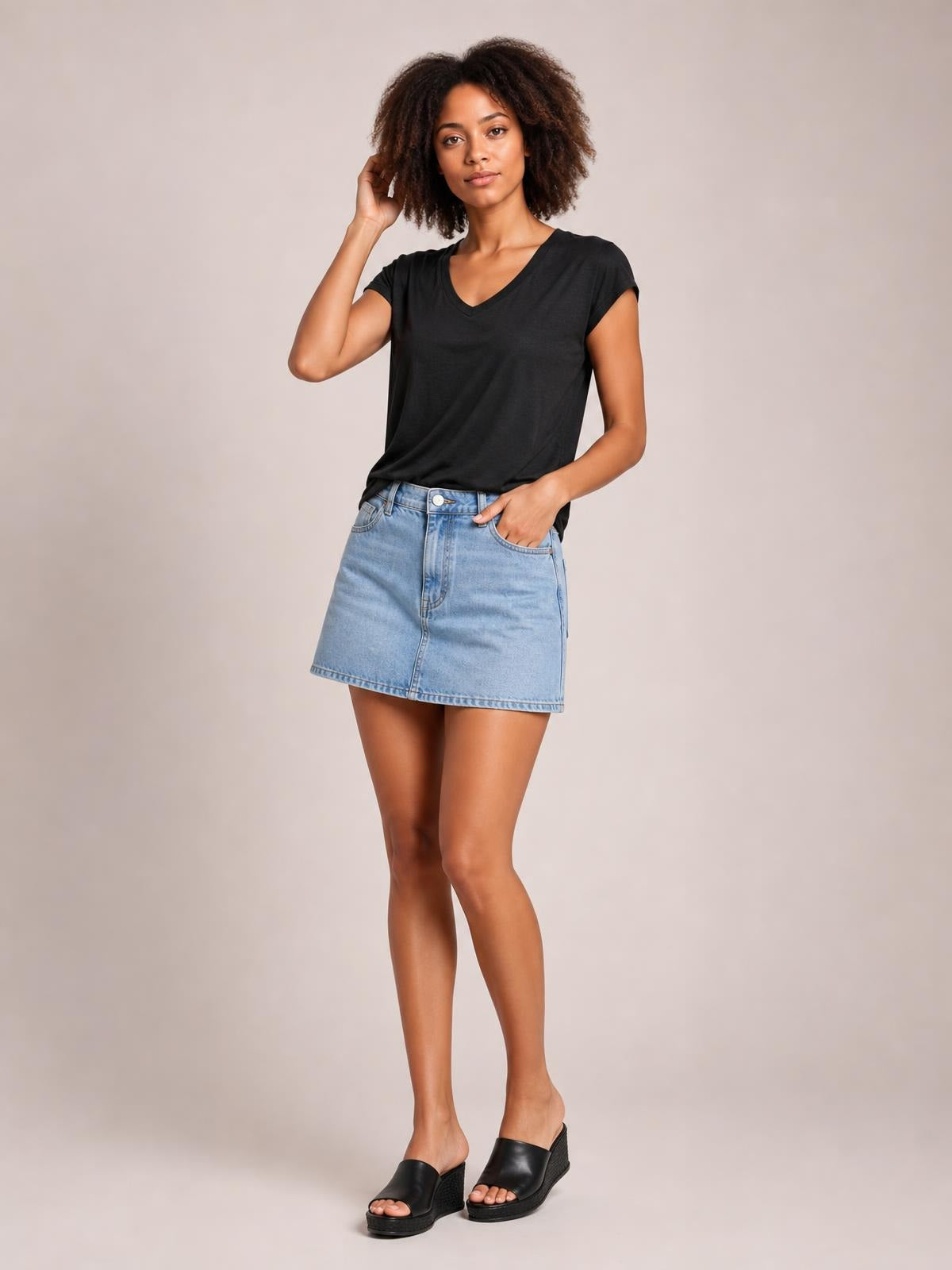 A model poses in a black V-neck short sleeve T-shirt with a relaxed straight silhouette, tucked into a light denim skirt.
