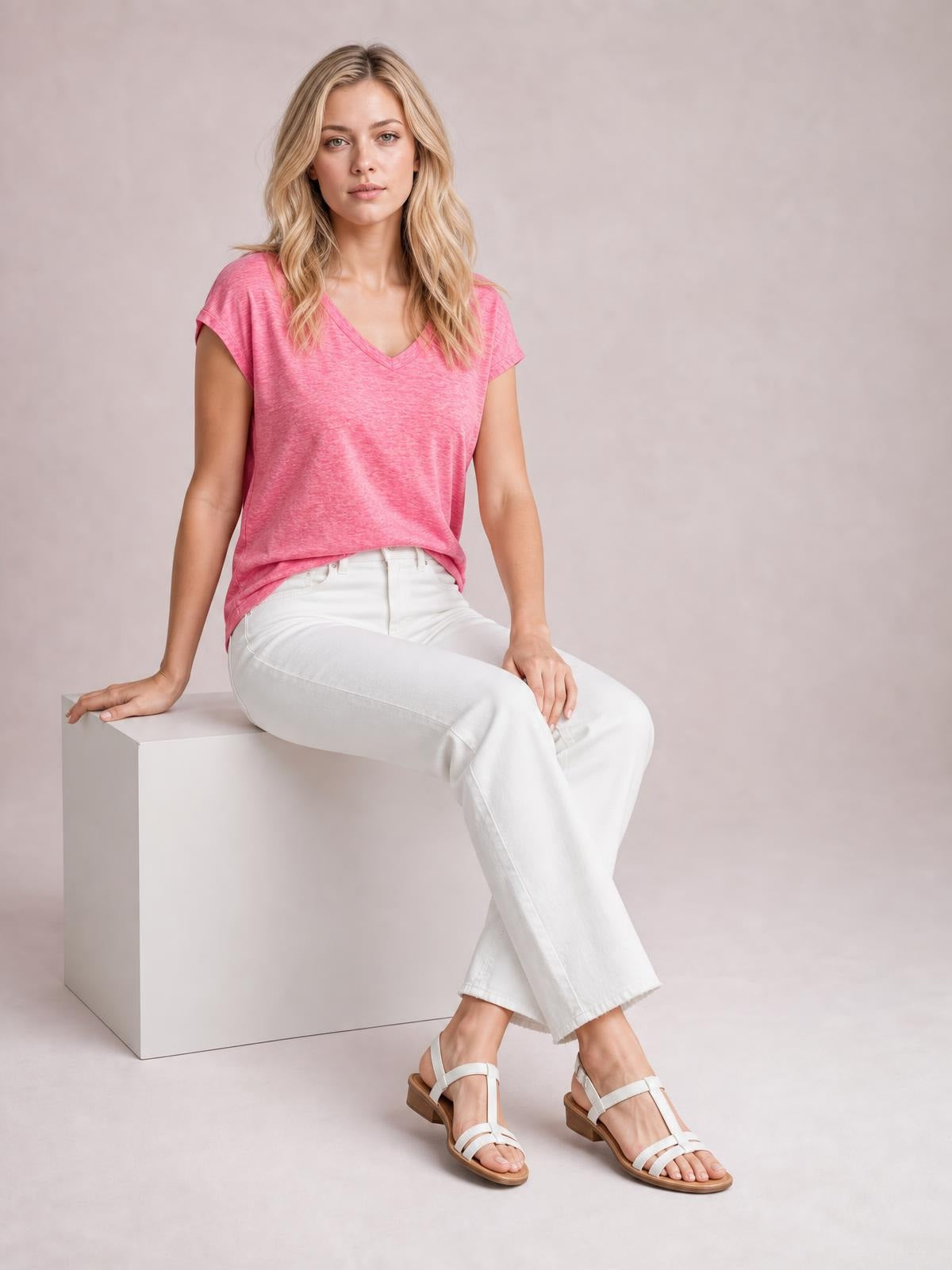 Model seated and wearing a pink V-neck short sleeve T-shirt with a relaxed basic silhouette, short sleeves, and a straight hem.