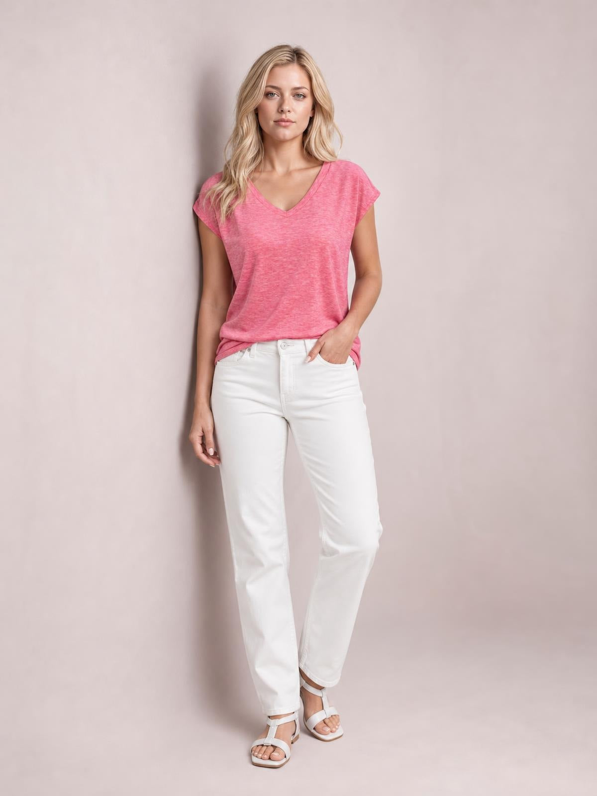 A model wears a pink V-neck short sleeve T-shirt with a relaxed, straight silhouette, standing with one hand in her jeans pocket.