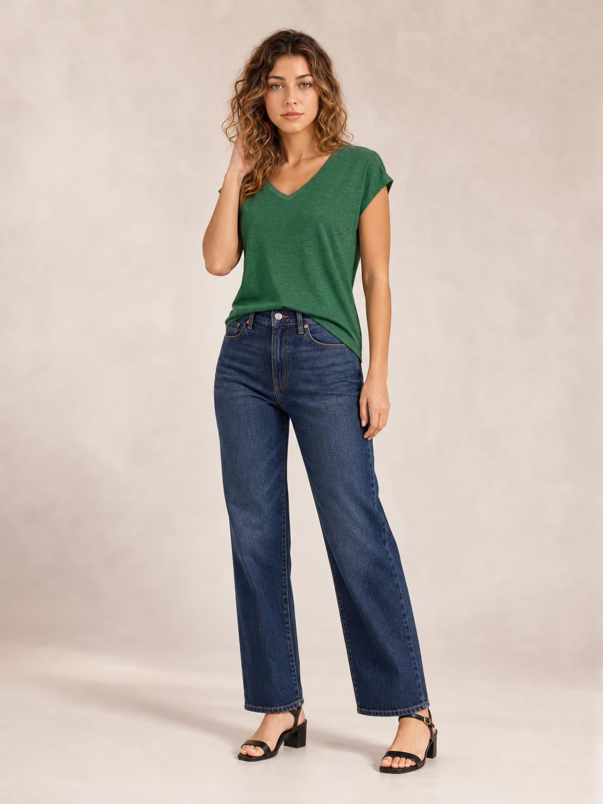 Model poses in a green V-neck short sleeve T-shirt with a relaxed straight silhouette and clean basic construction, paired with jeans.