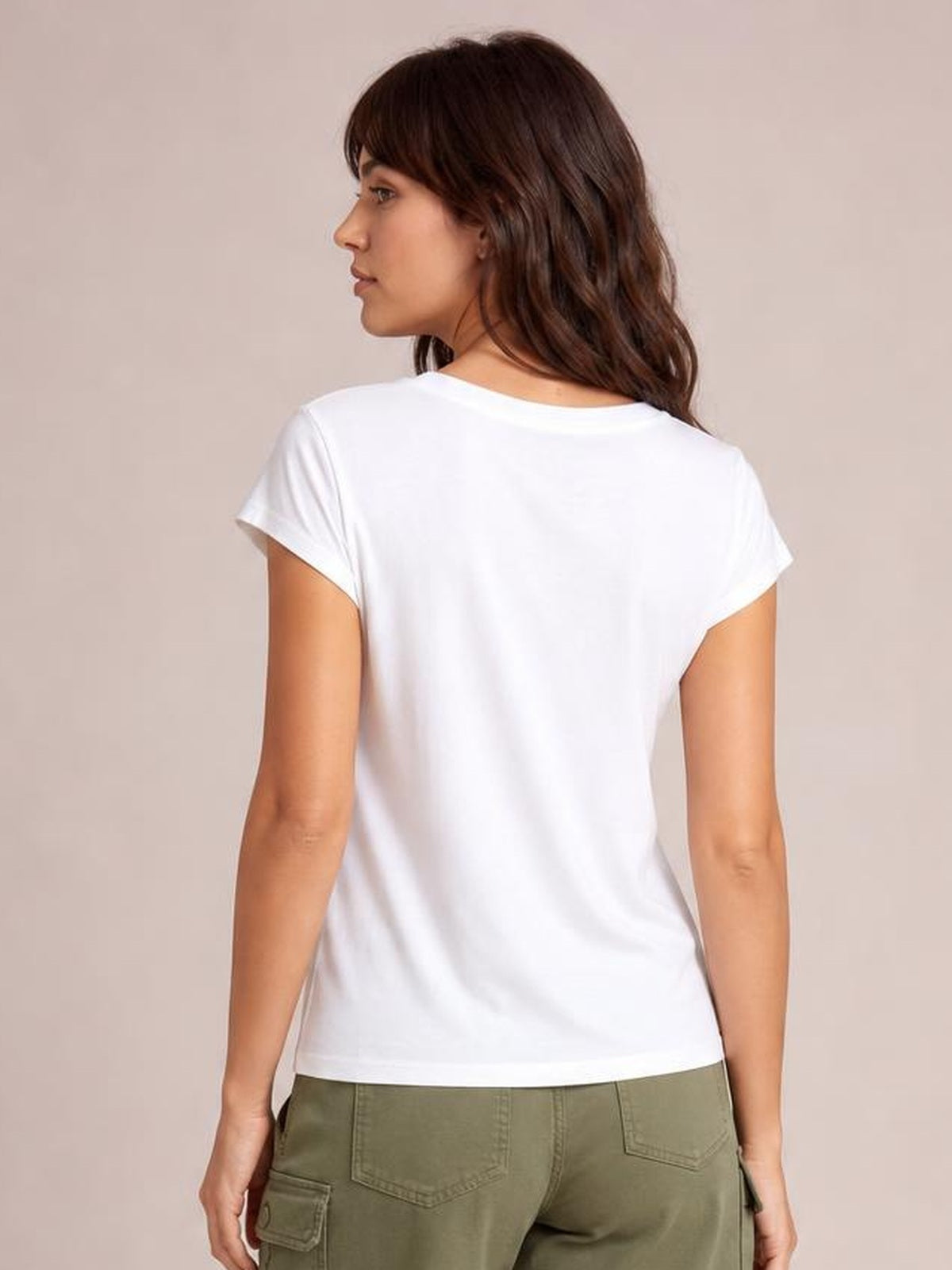 A model looks over her shoulder wearing a white short-sleeve V-neck T-shirt with a relaxed straight silhouette, smooth opaque fabric, and a clean hem.