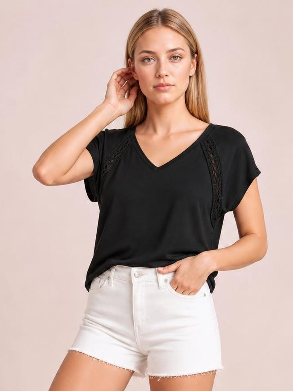 Model poses in a black V-neck short sleeve T-shirt with vertical eyelet details, a relaxed silhouette, and one hand resting near her hip.