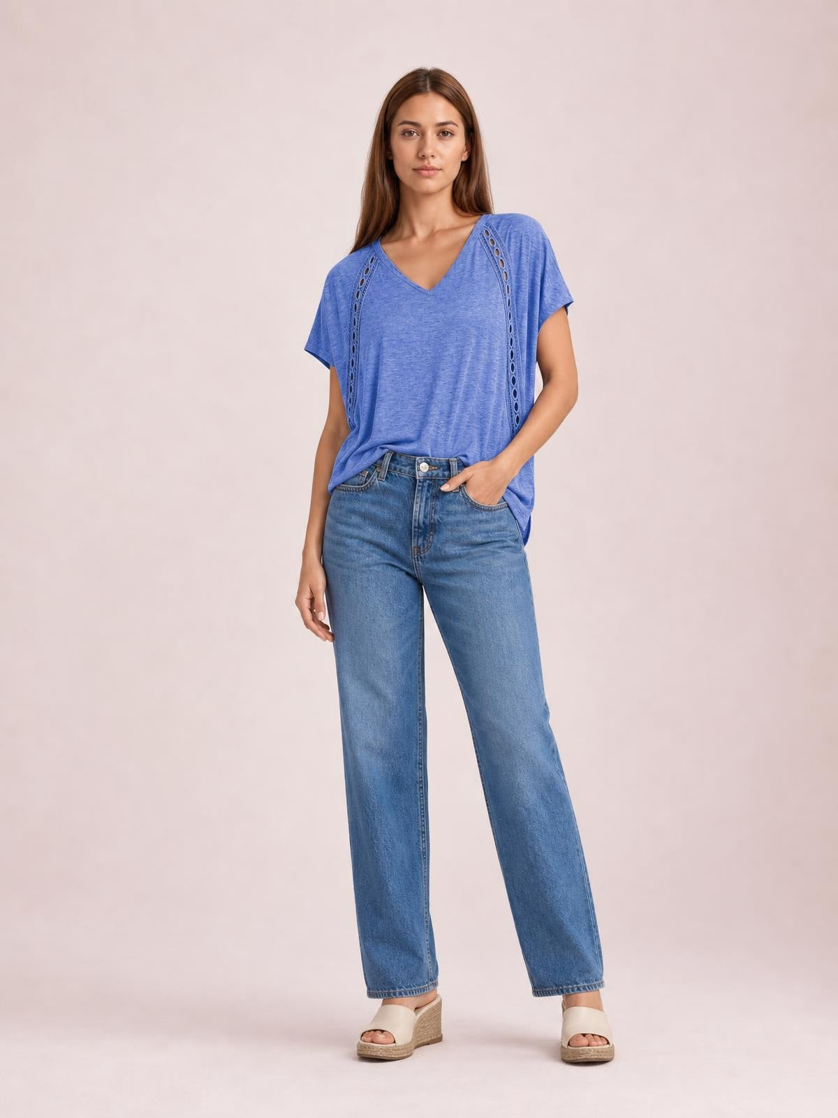 A model stands in a relaxed blue V-neck short sleeve T-shirt with vertical eyelet details and a loose, softly draped silhouette.