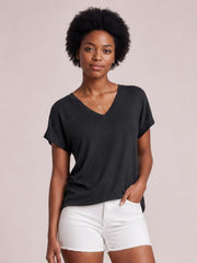 Model wears a black V-neck short sleeve T-shirt with a relaxed, slightly loose silhouette and smooth basic construction, posing with one hand in her pocket.