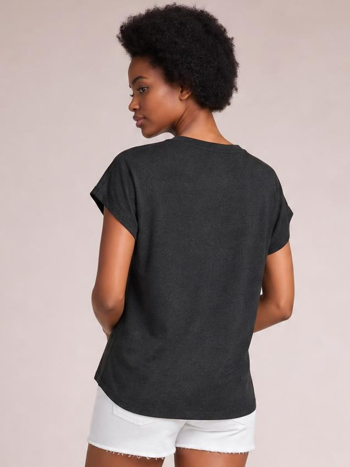 Model turns to show the back of a charcoal V-neck short sleeve T-shirt with a relaxed silhouette, straight hem, and rolled sleeve cuffs.