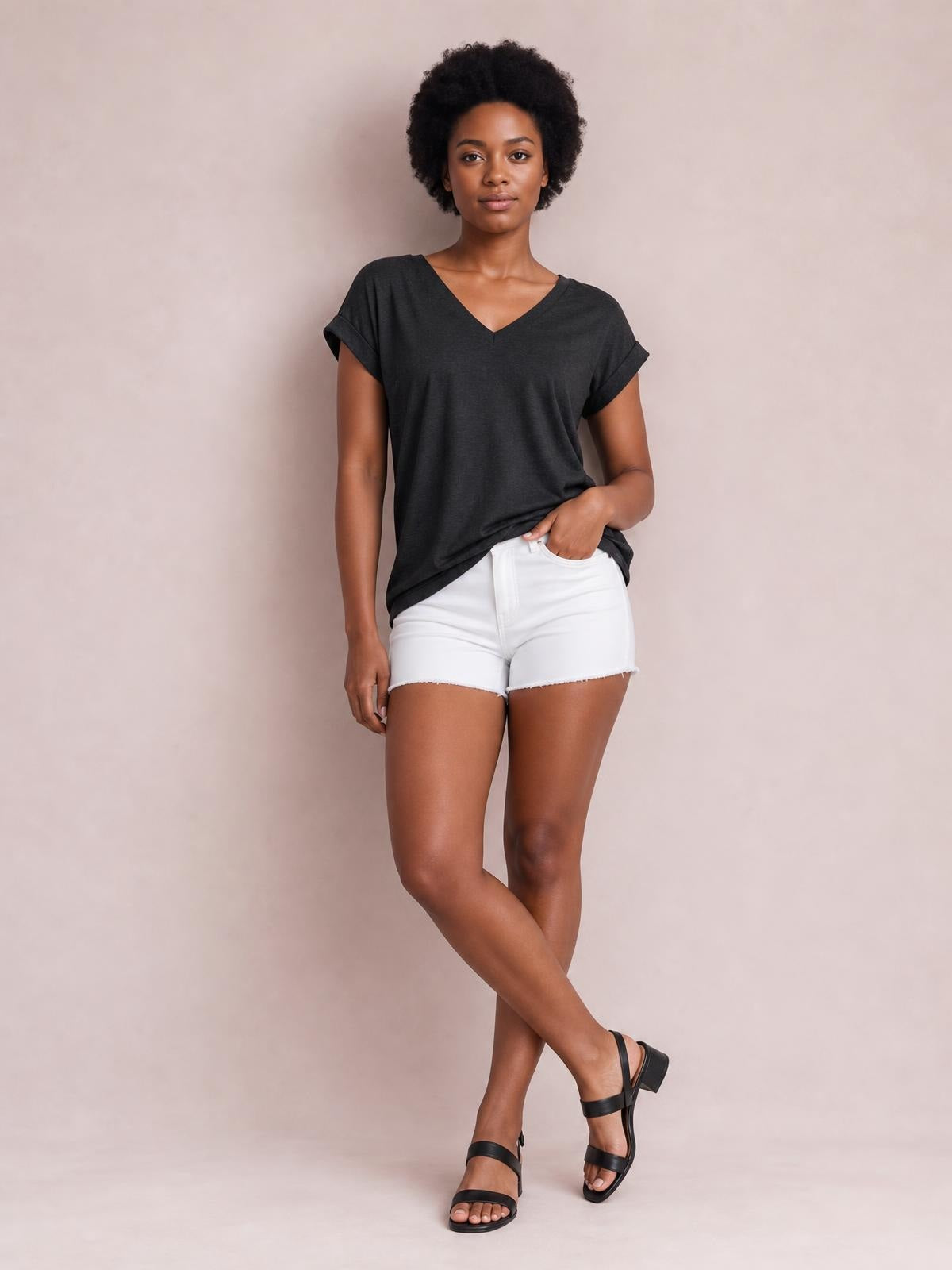 Model wearing a charcoal V-neck short sleeve T-shirt with rolled cuffs and a relaxed straight silhouette, posed with one hand in her pocket and legs crossed.