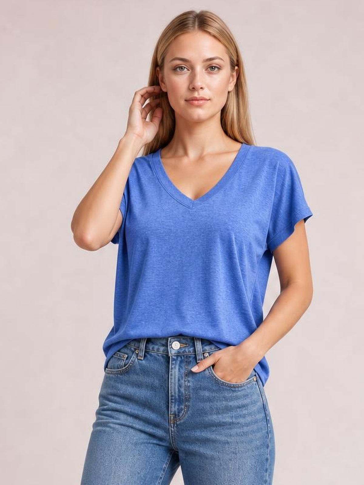 Model wearing a blue V-neck short sleeve T-shirt with a relaxed silhouette and finished neckline, posed with one hand in her jeans pocket.