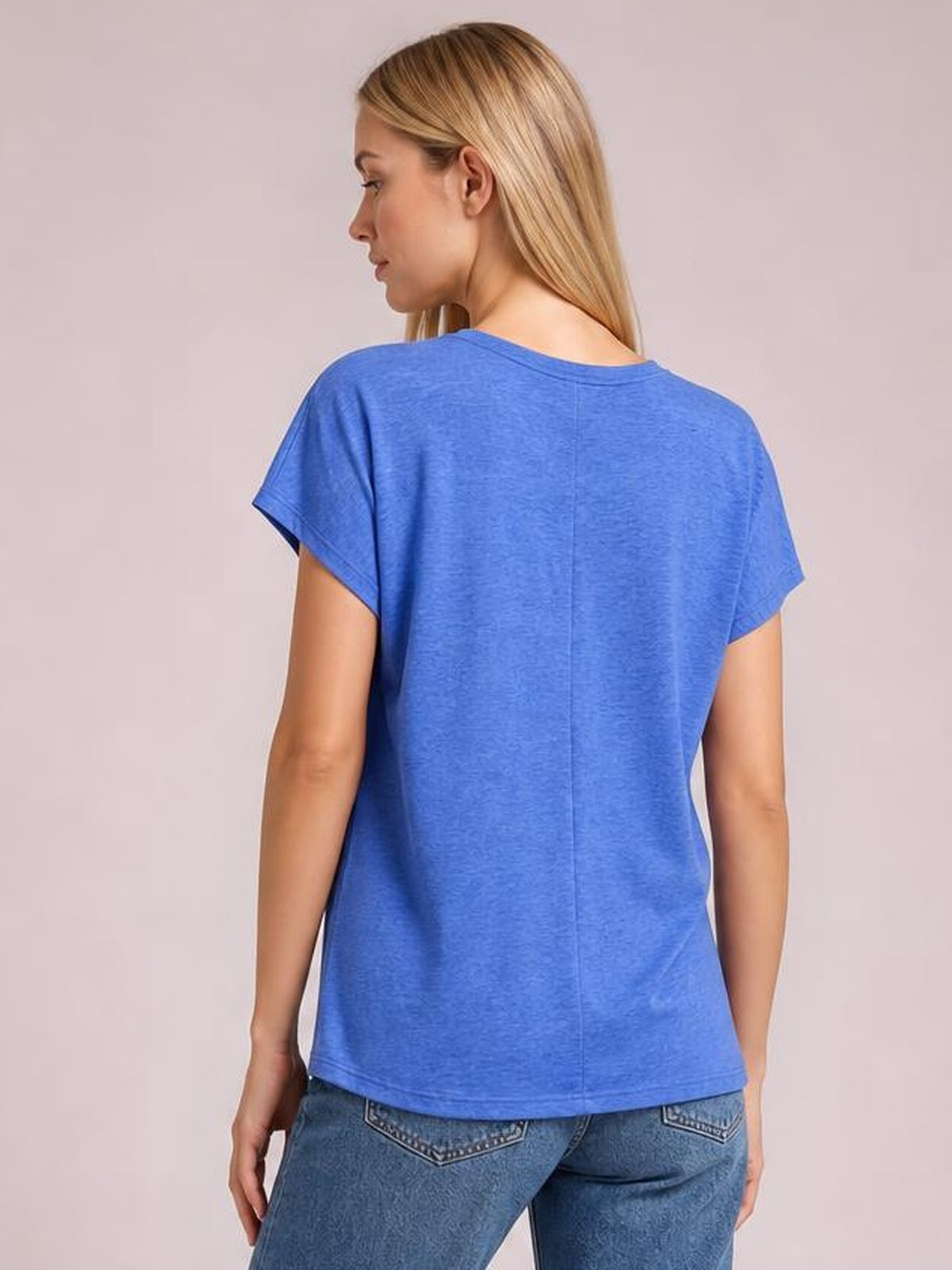 Model turned to show the back of a blue V-neck short sleeve T-shirt with a relaxed silhouette, cuffed sleeves, straight hem, and center back seam.