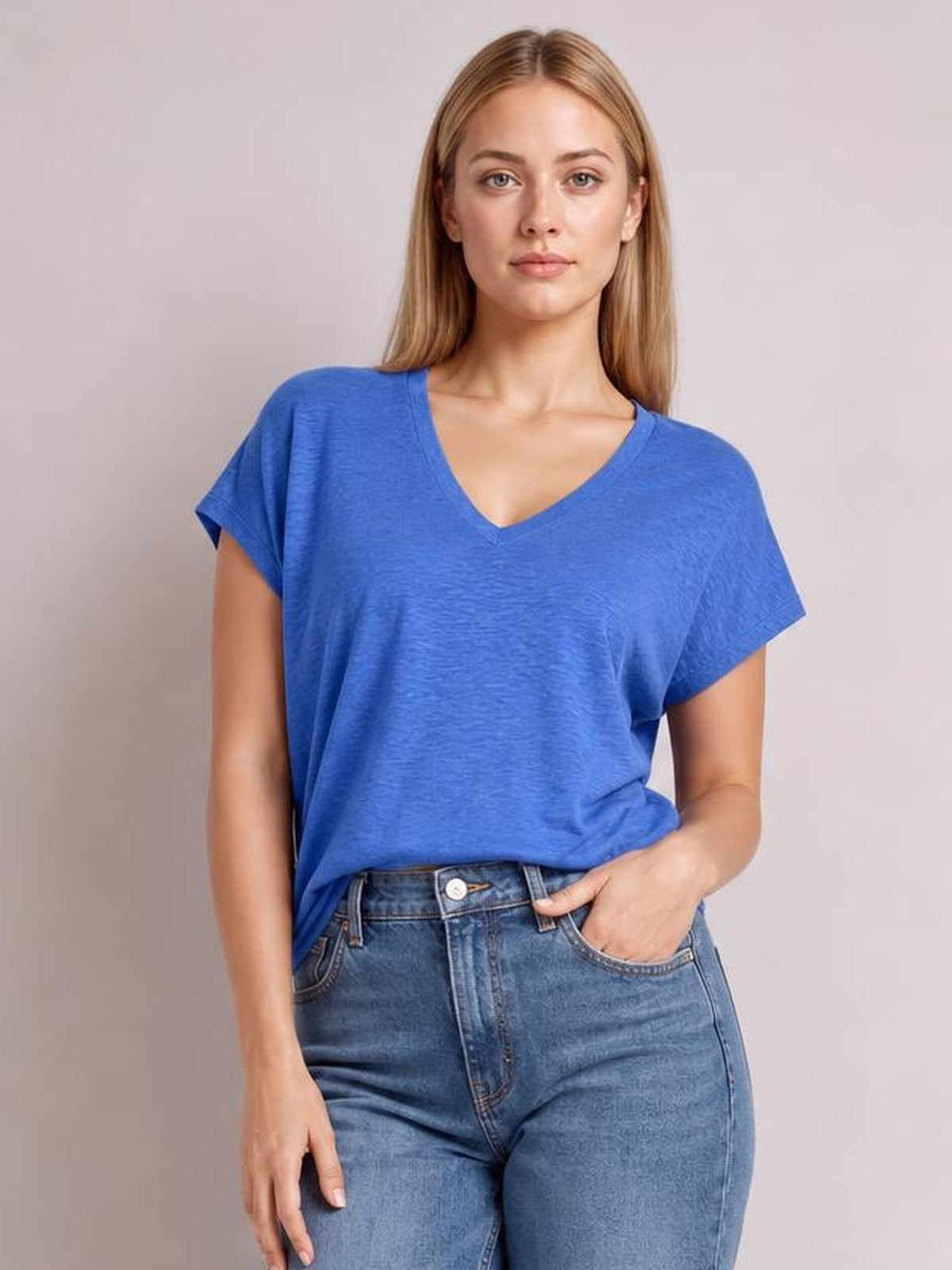 Model poses in a bright blue V-neck short sleeve T-shirt with a relaxed silhouette, softly draped fabric, and a slight front tuck into jeans.