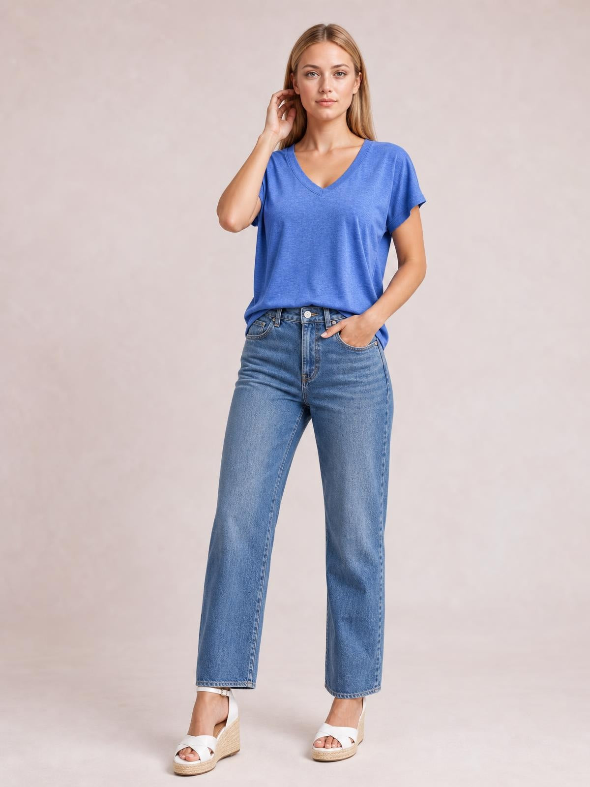 A woman poses in a blue V-neck short sleeve T-shirt with a relaxed straight silhouette, finished neckline and sleeve hems, one hand touching her hair.