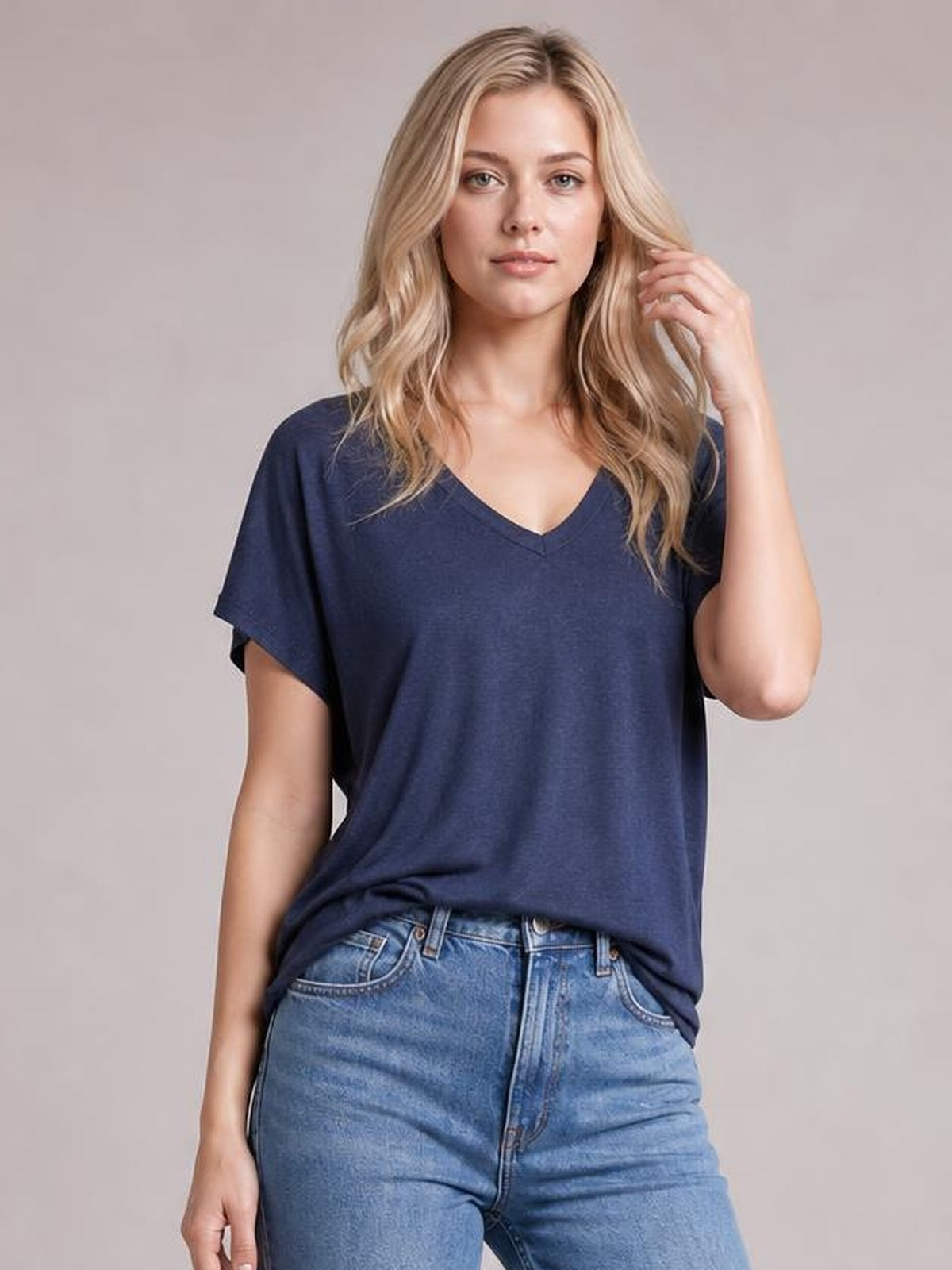 Model wearing a navy V-neck short sleeve T-shirt with a relaxed silhouette and draped hem, gently touching her wavy hair.