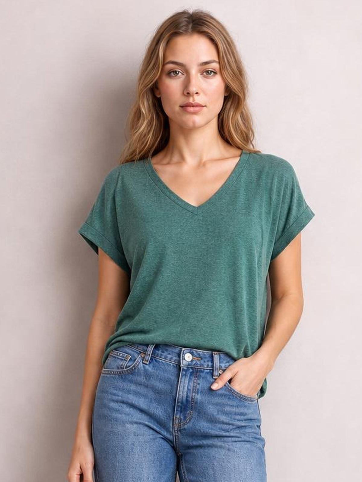 A model stands facing forward in a teal V-neck short sleeve T-shirt with cuffed sleeves, a relaxed silhouette, and a slightly tucked hem.