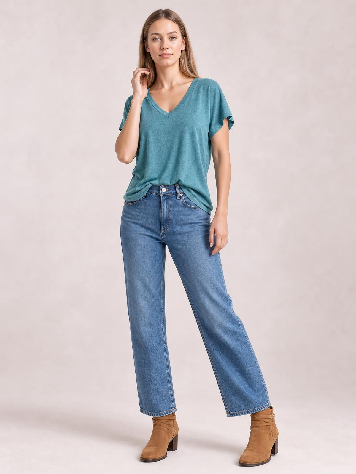Model wearing a teal V-neck short sleeve T-shirt with a relaxed silhouette and slight drape, standing with one hand near her hair.