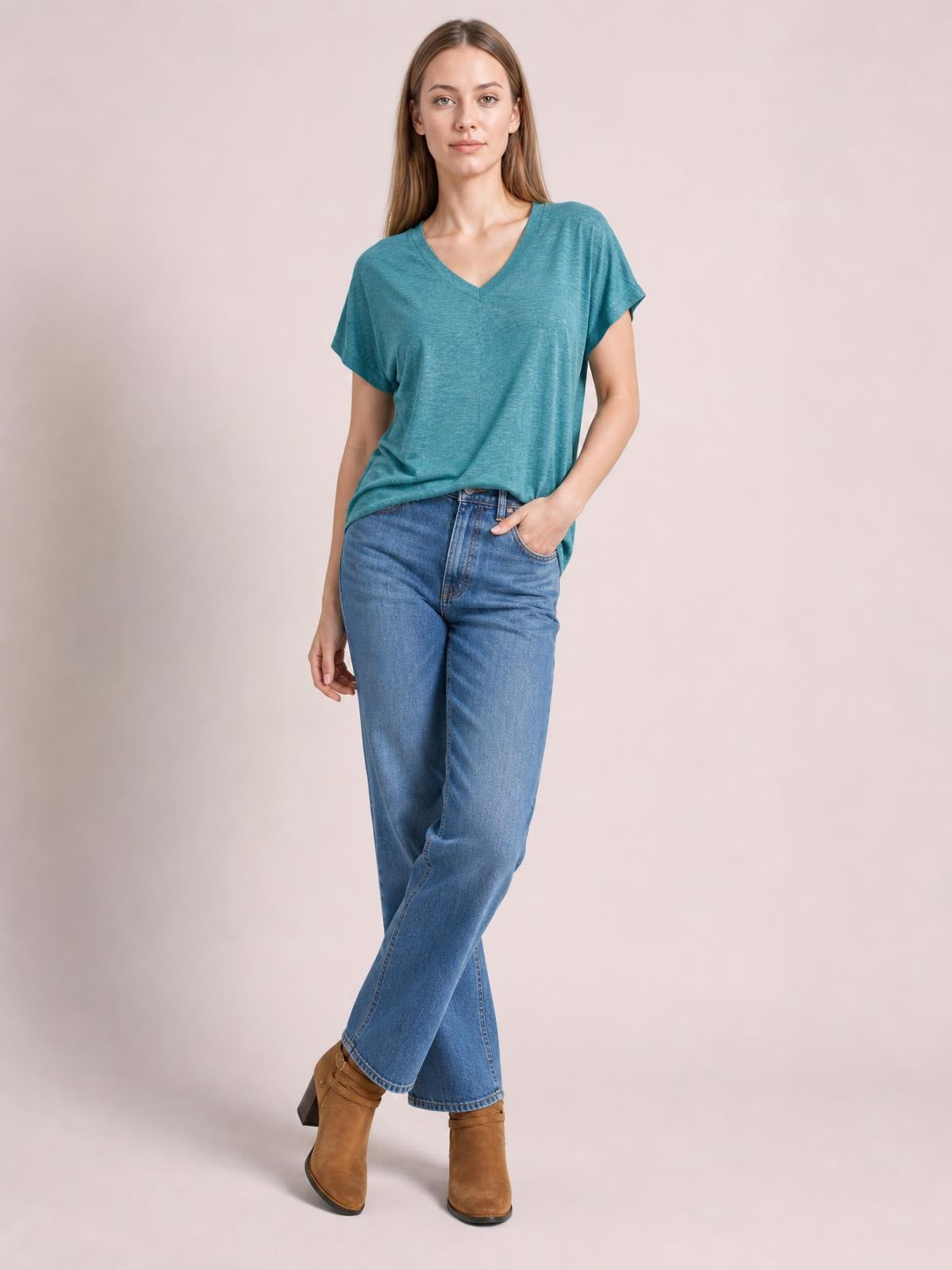 Model poses in a teal V-neck short sleeve T-shirt with a relaxed silhouette, paired with jeans and one hand tucked into a pocket.