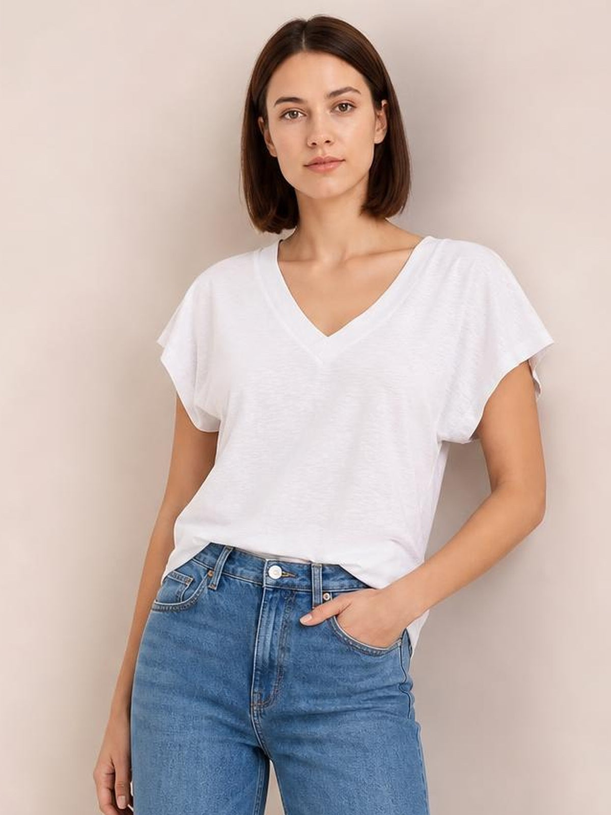 Model wearing a white V-neck short sleeve T-shirt with a relaxed silhouette and softly draped construction, posing with one hand in her jeans pocket.