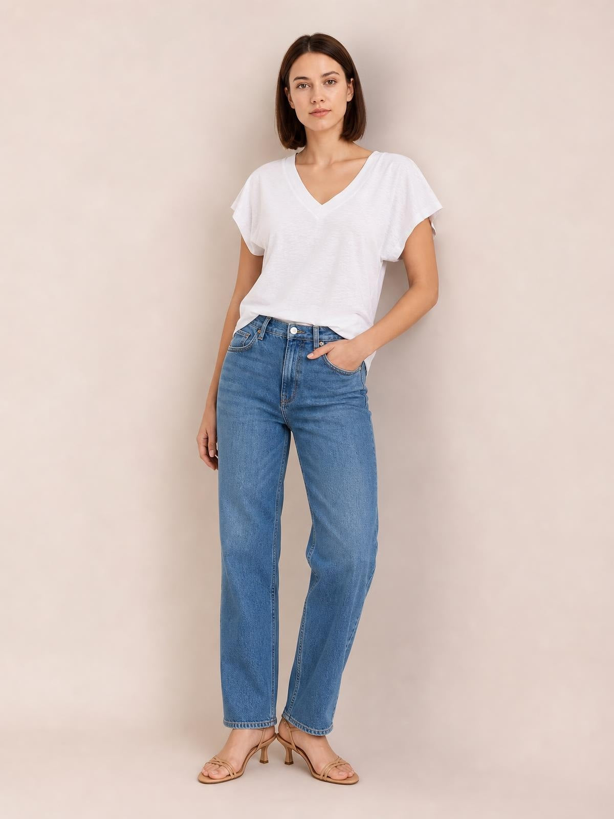 Model wearing a white V-neck short sleeve T-shirt with a relaxed silhouette and slightly draped construction, paired with jeans and heels.