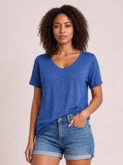Model wearing a blue V-neck short sleeve T-shirt with a relaxed straight silhouette, visible stitched neckline, and slightly draped hem over denim shorts.