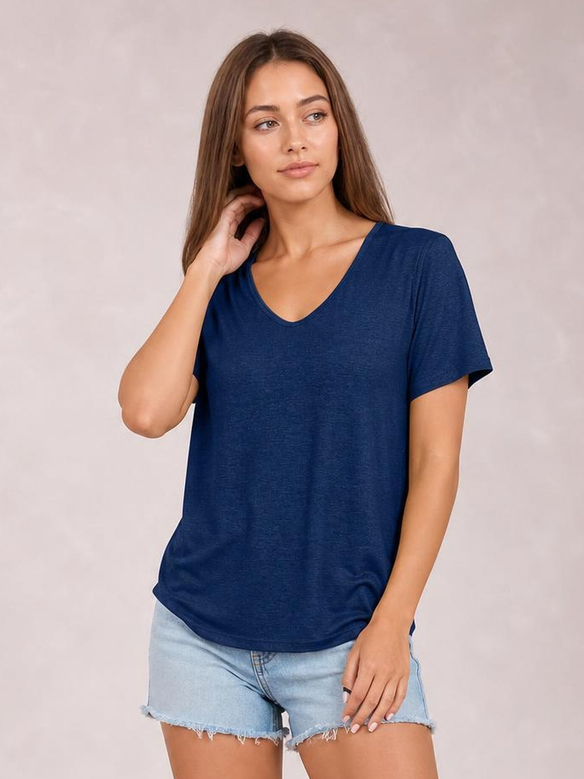 Model wearing a navy V-neck short sleeve T-shirt with a relaxed straight silhouette and curved hem, posing with one hand near her hair.