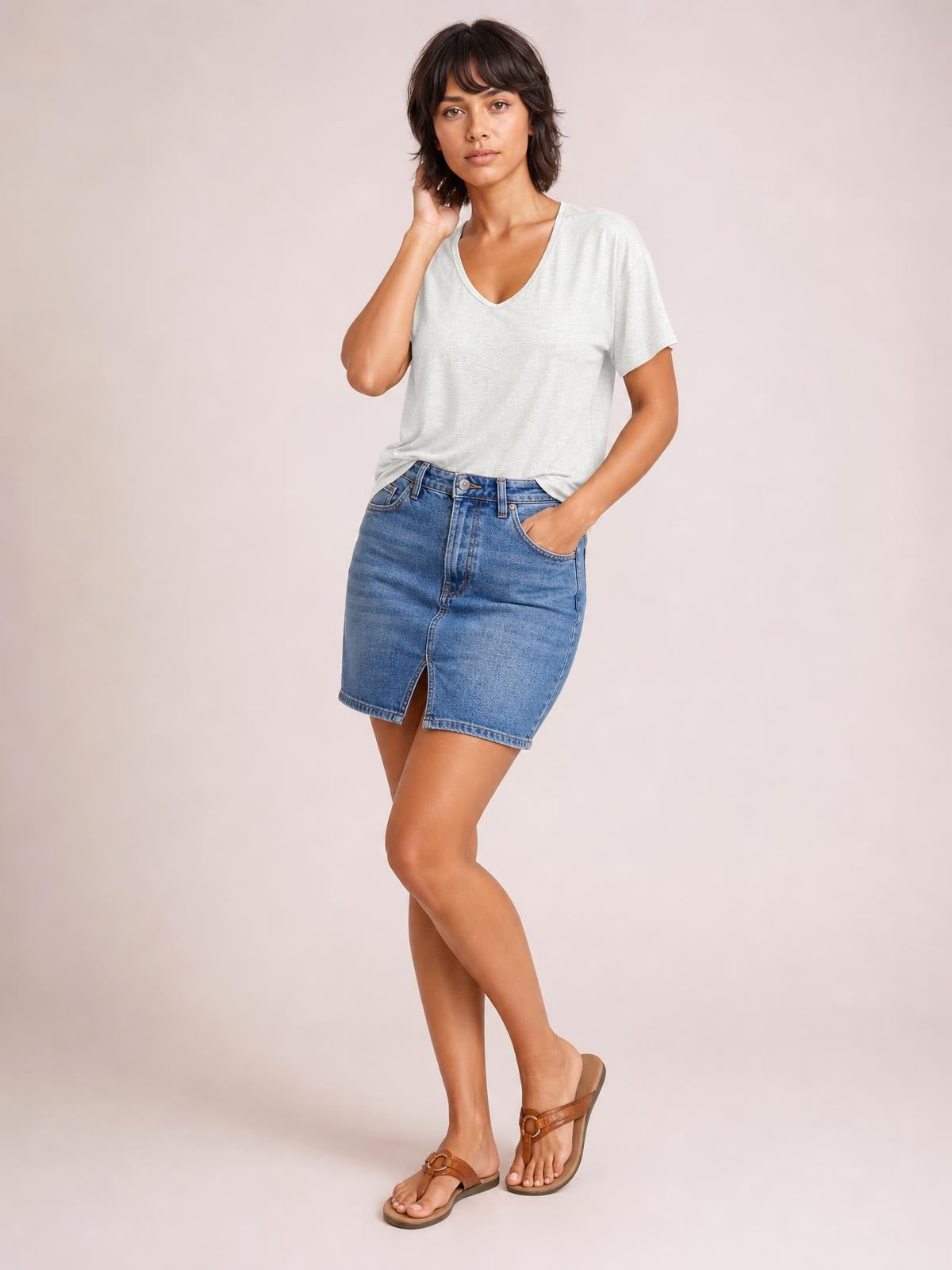Model wearing an opaque light gray V-neck short sleeve T-shirt with a relaxed silhouette and subtly finished neckline, posed with one hand in her pocket.