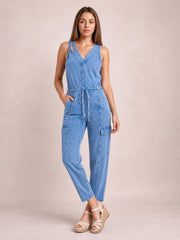 Model poses in a light blue sleeveless denim jumpsuit with a V-neck, adjustable drawstring waist, cargo-style pockets, and a relaxed tapered-leg silhouette.
