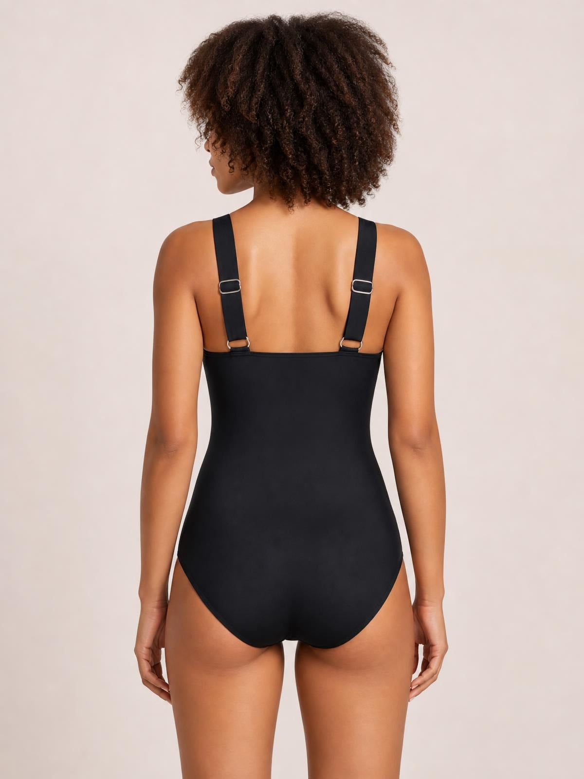 Back view of a model wearing a black sleeveless one-piece swimsuit with a smooth fitted silhouette, open back, and adjustable shoulder straps with metal buckles.