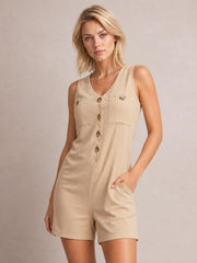 Model poses in a beige V-neck sleeveless romper with a relaxed silhouette, button-front closure, chest patch pockets, and convenient side pockets.
