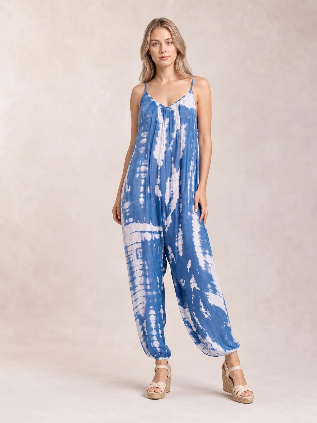 A model stands in a blue-and-white tie-dye V-neck spaghetti strap jumpsuit with a relaxed wide-leg silhouette and elasticized ankle cuffs.