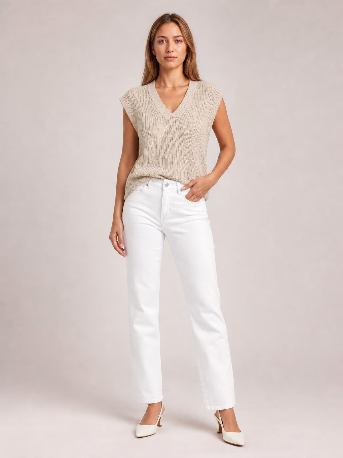 Model stands with one hand in her pocket wearing a light beige V-neck sweater vest with a ribbed knit, sleeveless cut, relaxed silhouette, and bound neckline.