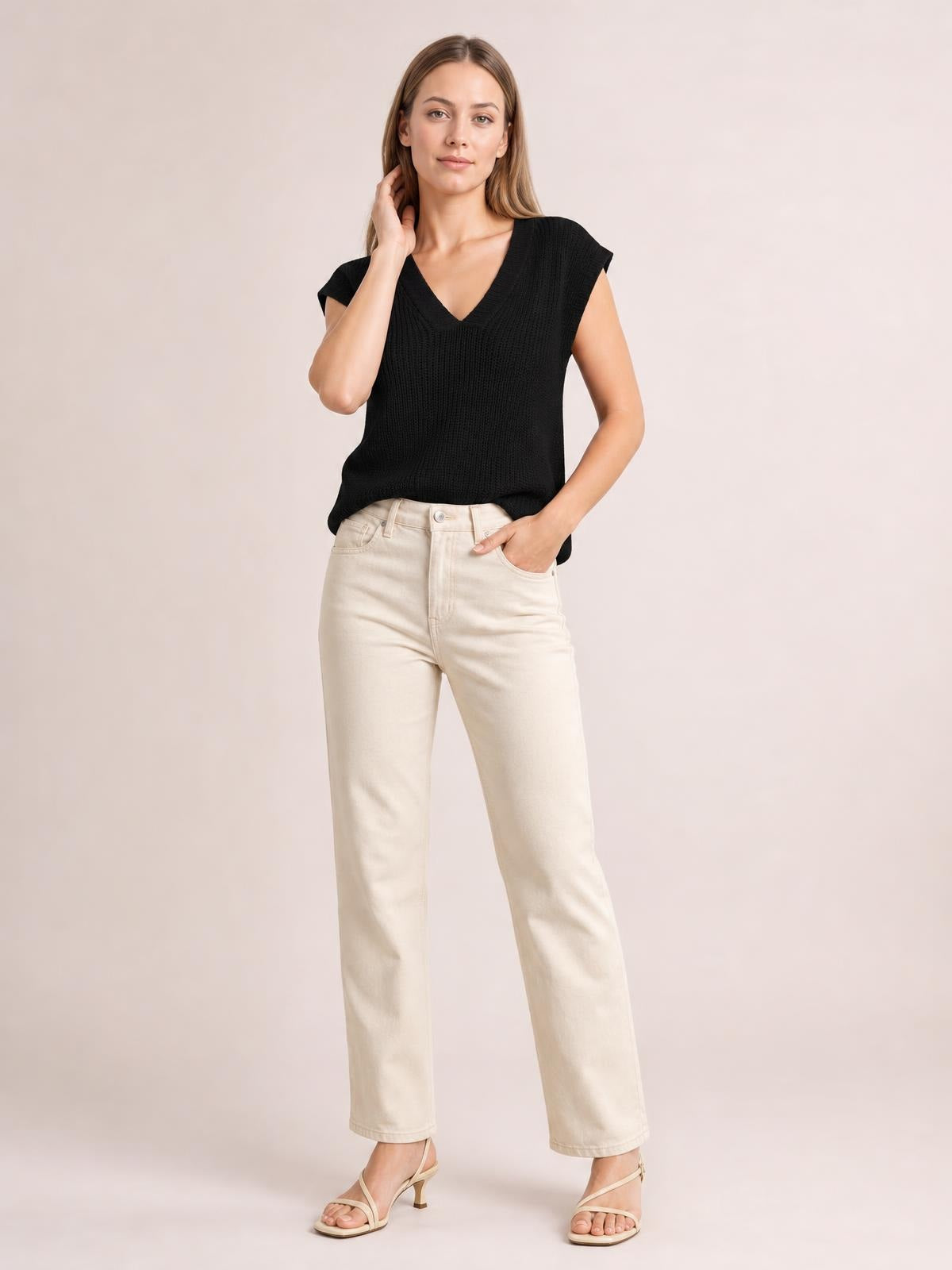 A model poses in a black V-neck sweater vest with ribbed knit construction, sleeveless cut, and relaxed straight silhouette, paired with cream jeans.