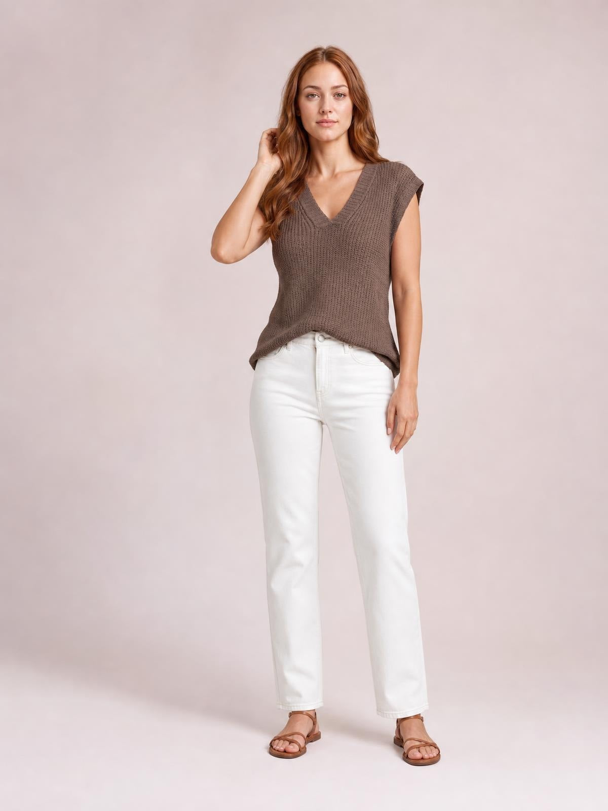 Model wearing a taupe V-neck sweater vest with ribbed trim, sleeveless silhouette, and relaxed straight fit, posed with one hand touching her hair.