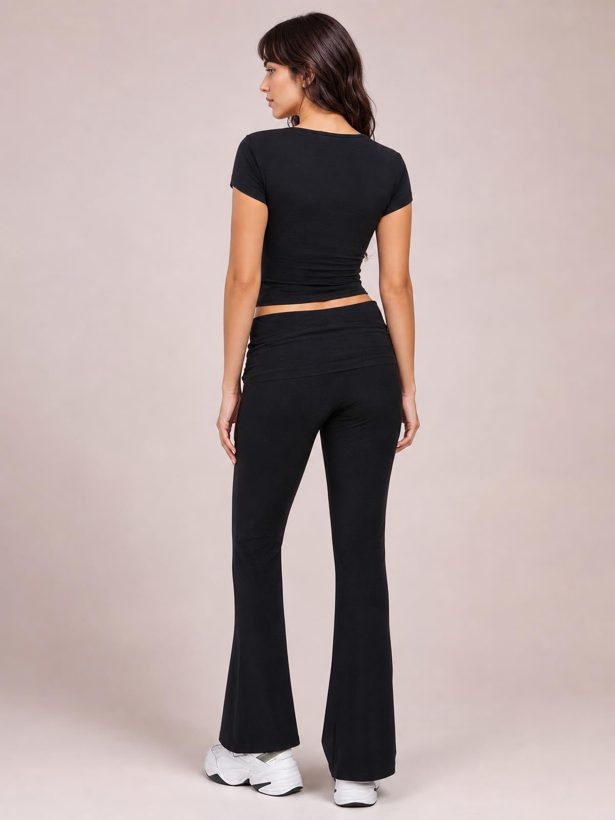 A model faces away in a black short-sleeve top and high-waisted bootcut leggings set, showing its fitted silhouette and flared hems.