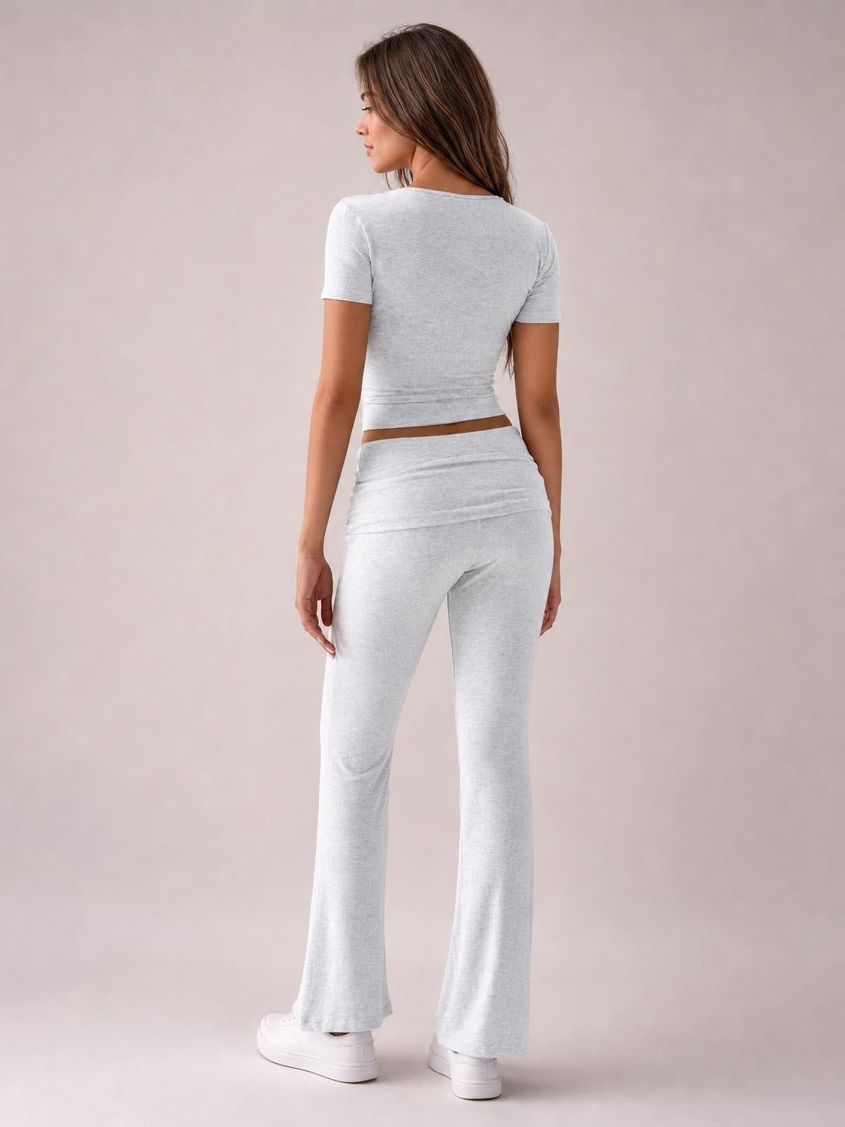 A model poses from the back in a light gray fitted short-sleeve top and matching bootcut leggings with a subtle flare and stretch silhouette.