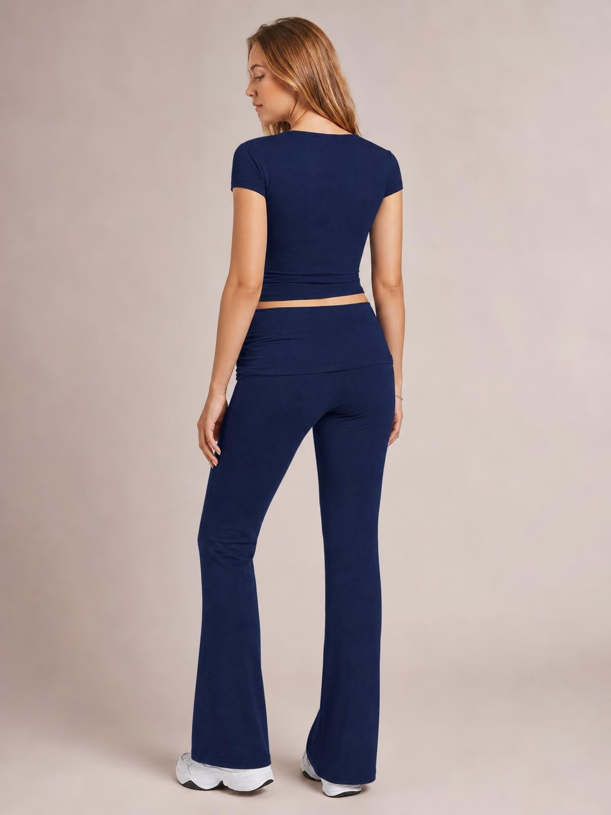 A model poses from the back in a navy short-sleeve top with a cropped hem and matching high-waisted bootcut leggings, creating a sleek, stretchy silhouette.