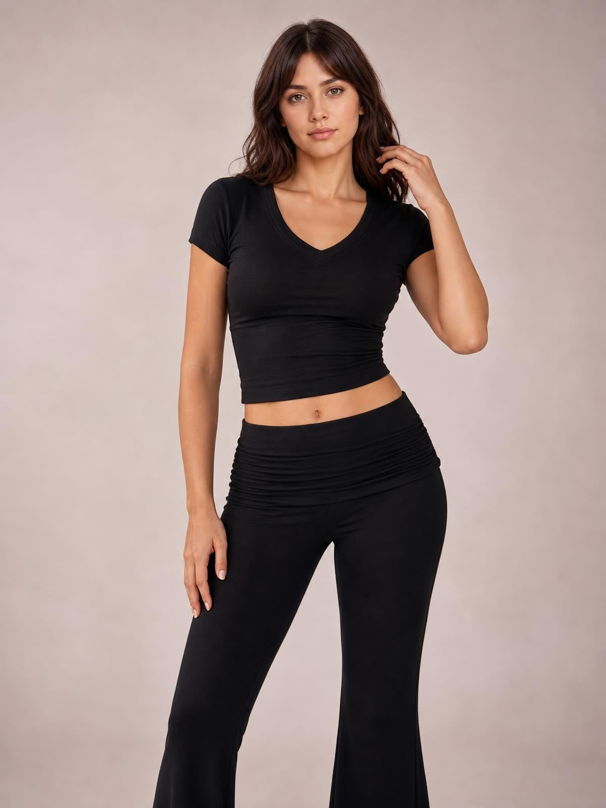 A model poses in a black V-neck top and matching high-waisted bootcut leggings, featuring a fitted silhouette and ruched waistband.