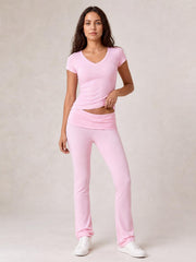 Model wearing a pink V-neck top and matching bootcut leggings with a fitted silhouette, wide waistband, and relaxed standing pose in white sneakers.