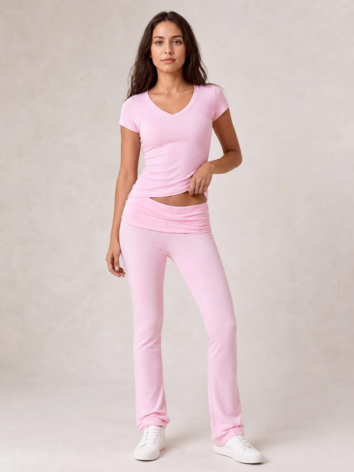Model wearing a pink V-neck top and matching bootcut leggings with a fitted silhouette, wide waistband, and relaxed standing pose in white sneakers.