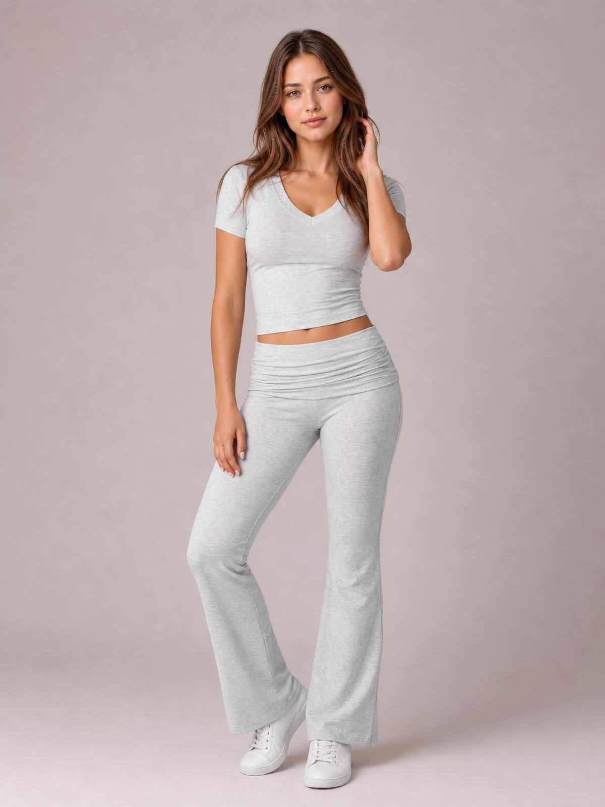 Model poses in a light gray V-neck top and matching high-waisted bootcut leggings, featuring a fitted silhouette, flared hems, and short sleeves.