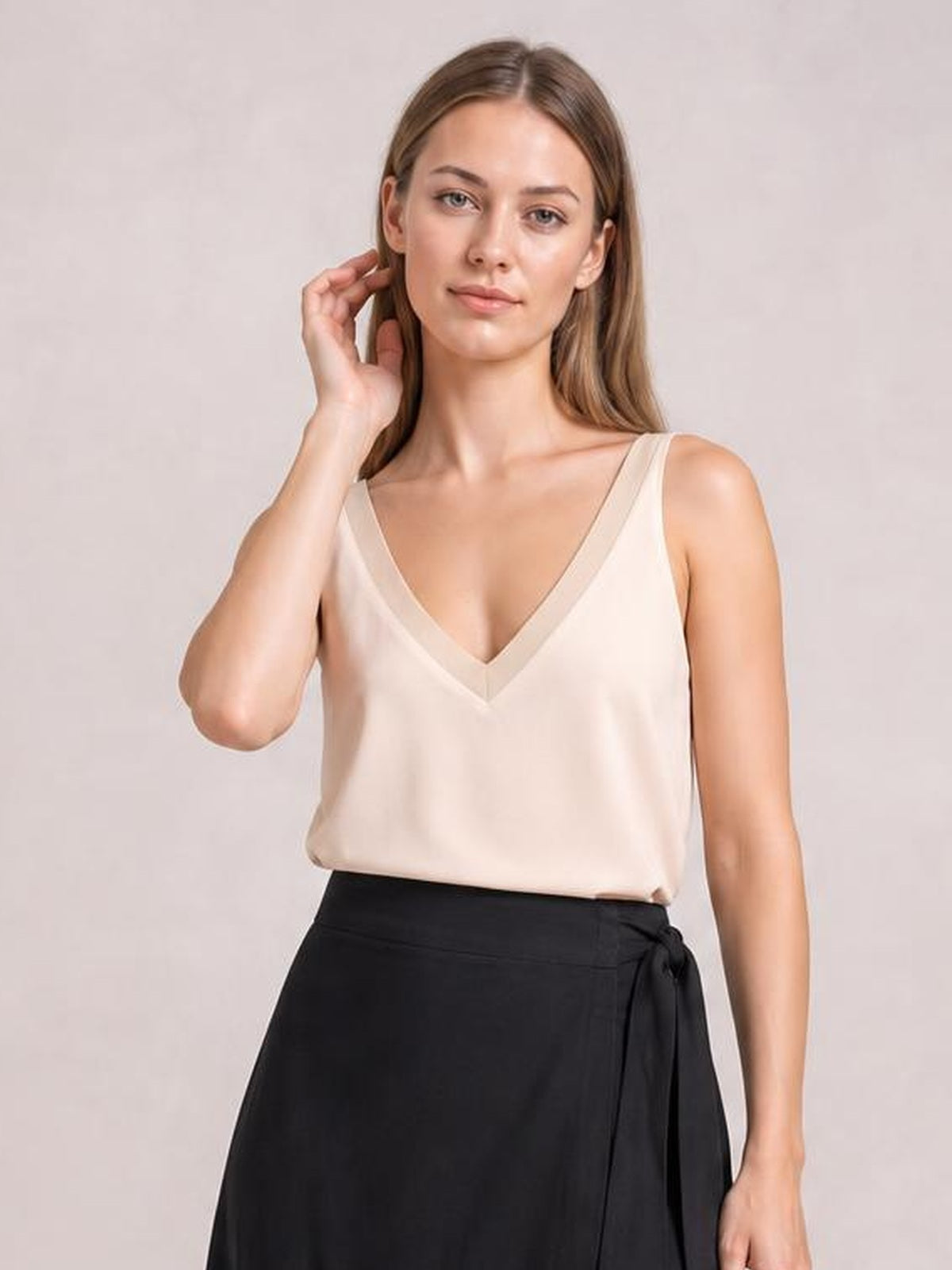 A model wears an ivory V-neck wide strap cami with a relaxed silhouette and subtle neckline trim, posing with one hand near her hair.