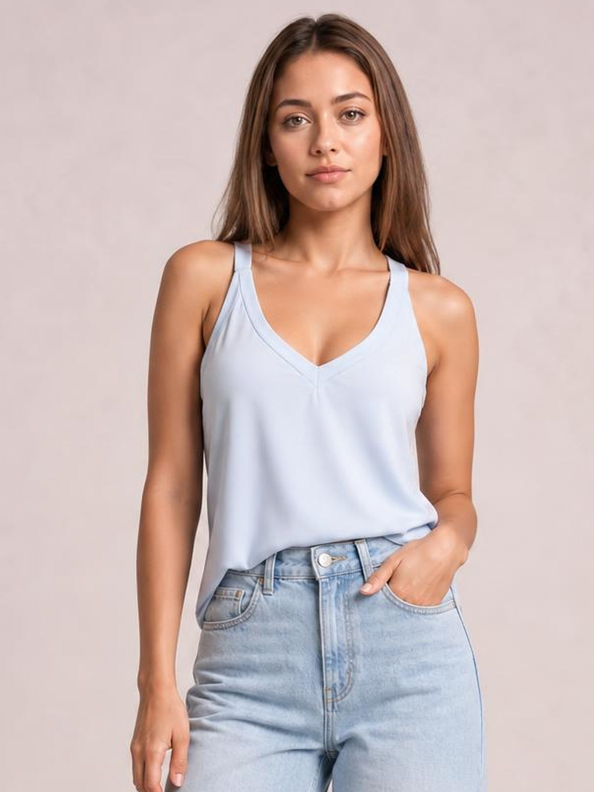 Model wears a light blue V-neck wide strap cami with a relaxed straight silhouette, softly draped fabric, and a front tuck into high-waisted jeans.