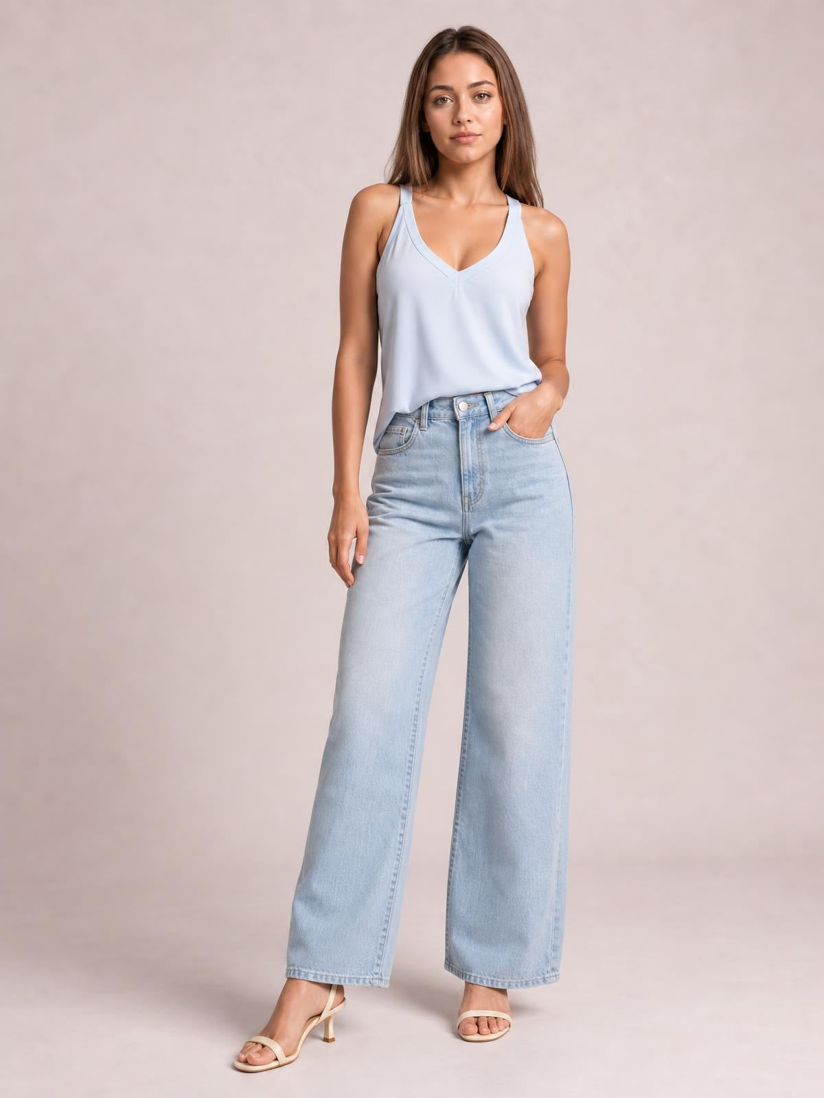 Model wearing a light blue V-neck wide strap cami with a relaxed silhouette, subtle front seam, and one hand tucked into wide-leg jeans.