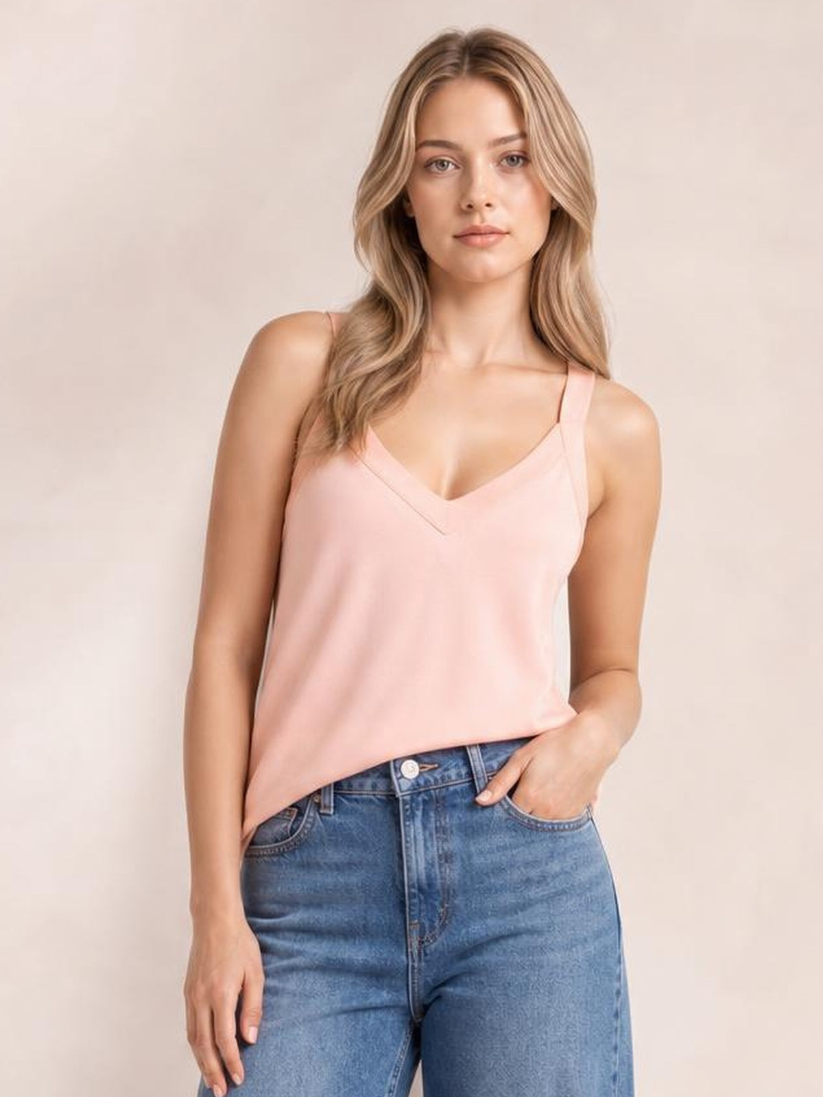 Model wearing a blush pink V-neck wide strap cami with a relaxed straight silhouette and clean seamed neckline, paired with blue jeans.