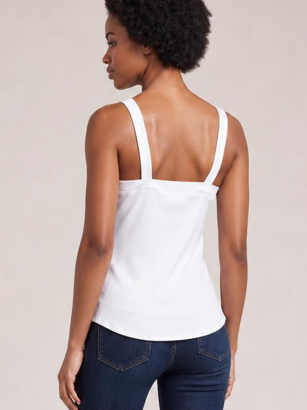 Model shown from the back wears a white wide-strap cami with a straight, relaxed silhouette, low back neckline, and gently curved hem.