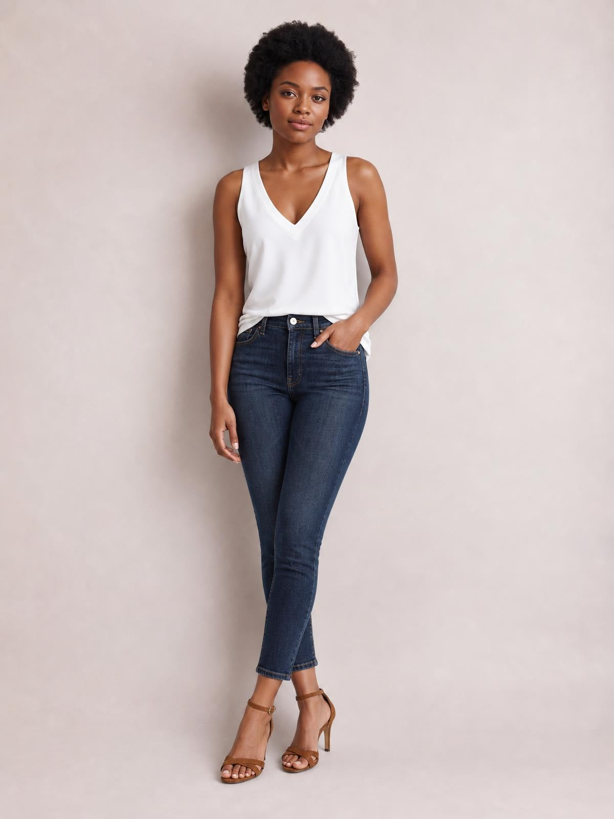 A model stands in a white V-neck wide strap cami with a relaxed straight silhouette, paired with dark blue jeans and one hand in her pocket.