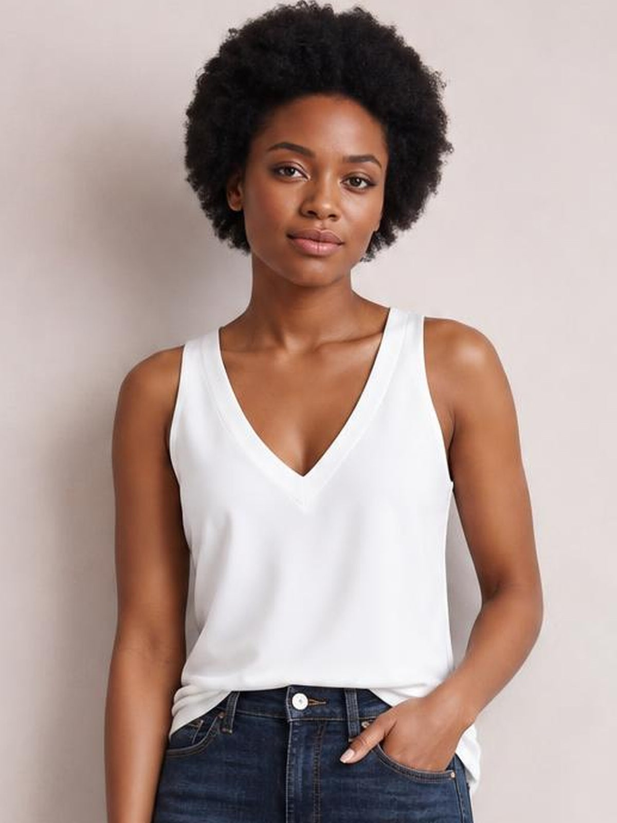 Model wears a white V-neck wide strap cami with a relaxed straight silhouette, standing front-facing with one hand in her jeans pocket.