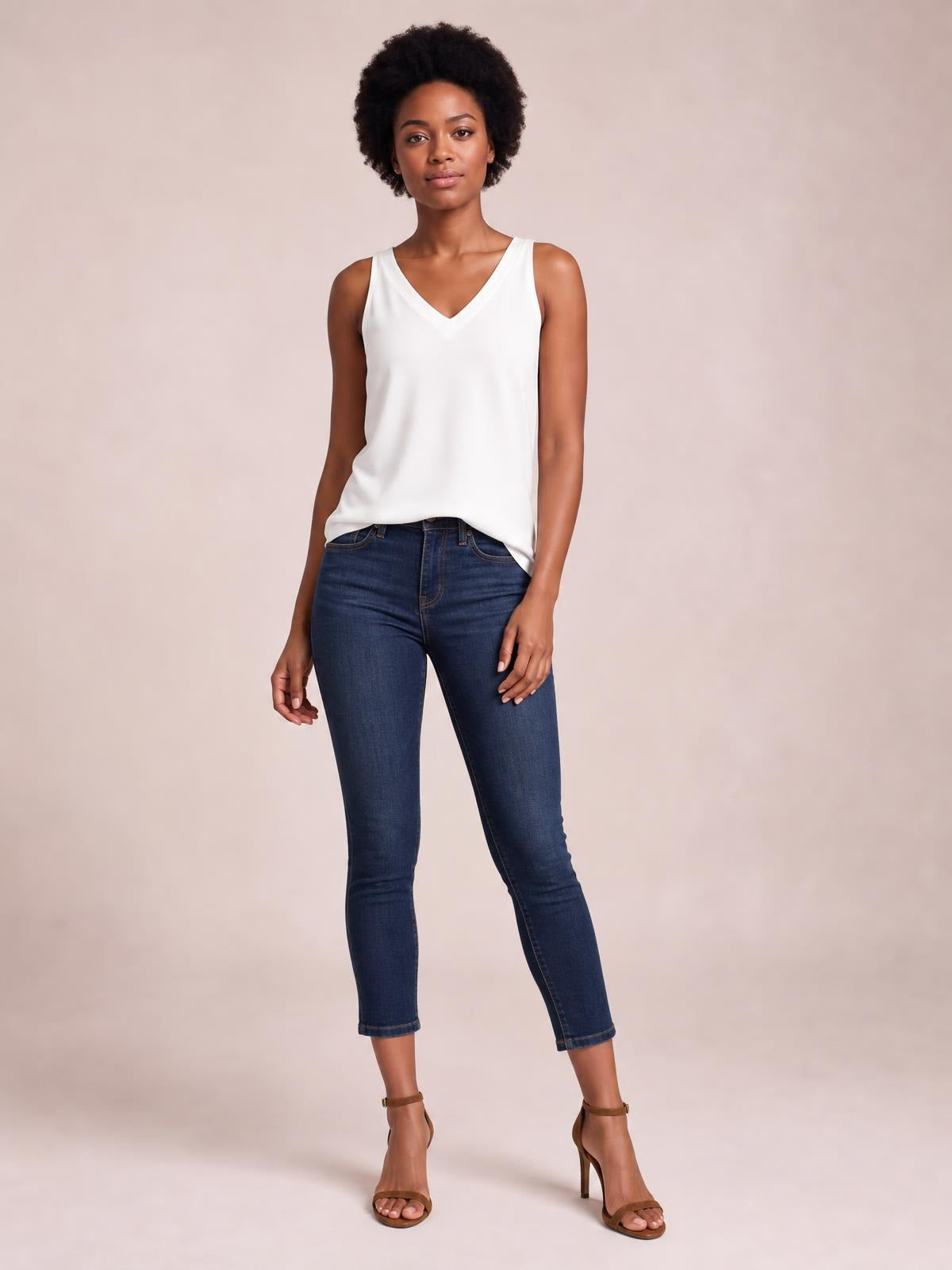 Model poses in a white V-neck wide strap cami with a relaxed straight silhouette and curved hem, paired with dark skinny jeans.