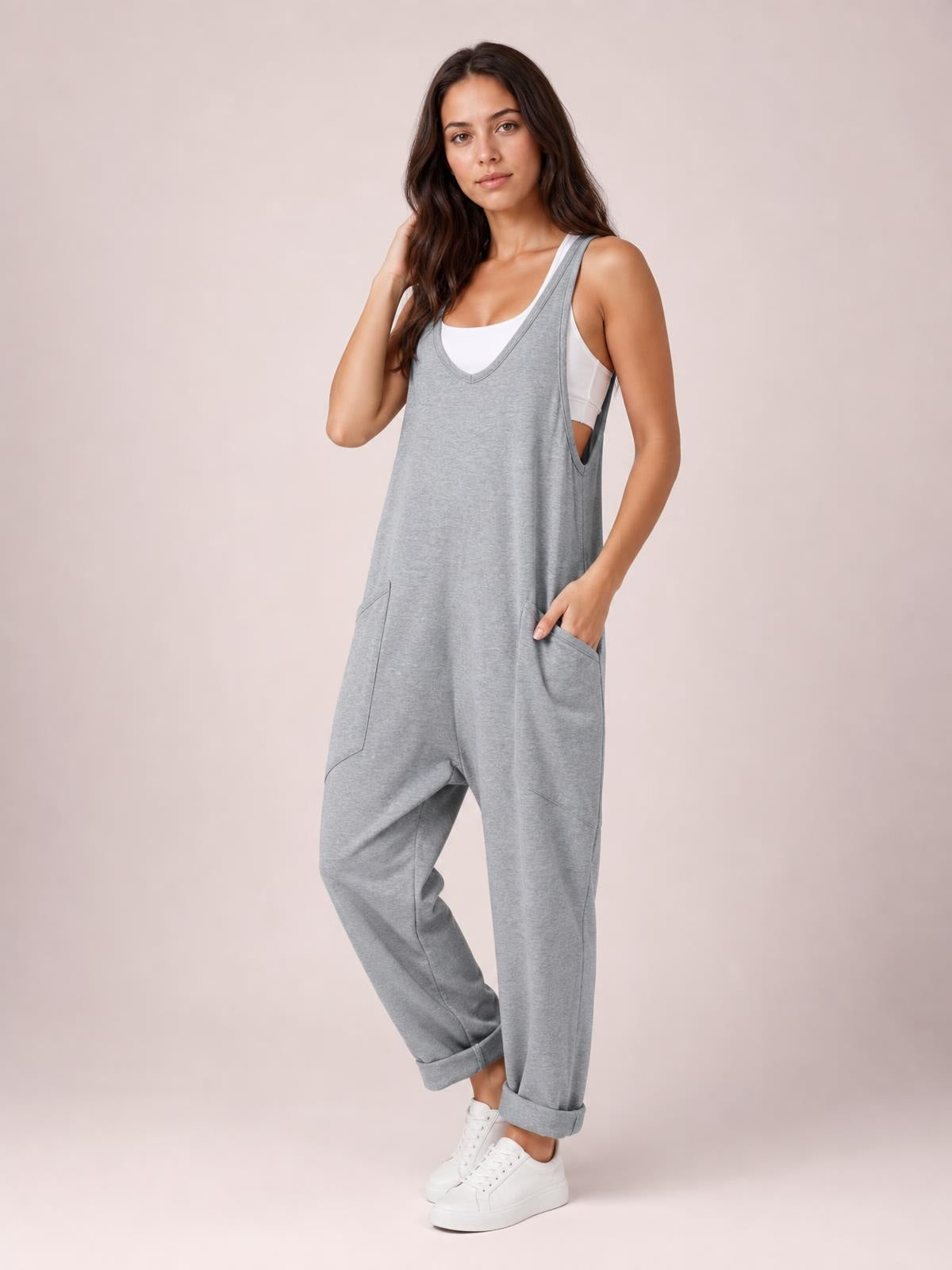 Model poses in gray V-neck wide-strap overalls with a relaxed, loose-fit silhouette, cuffed legs, and two front pockets over a white tank top.