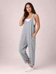 Model poses in gray V-neck wide-strap overalls with a relaxed, loose-fit silhouette, cuffed legs, and two front pockets over a white tank top.